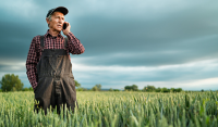 Rural Hospital Reduces No-Shows with a Boost in Patient Engagement. A farmer in overalls and a baseball cap stands in a crop field talking on his phone.